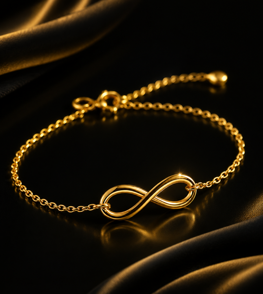 A gold chain bracelet featuring a polished infinity symbol centerpiece, displayed on a dark reflective surface with draped black fabric.